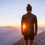 A person standing on top of a mountain at sunset.