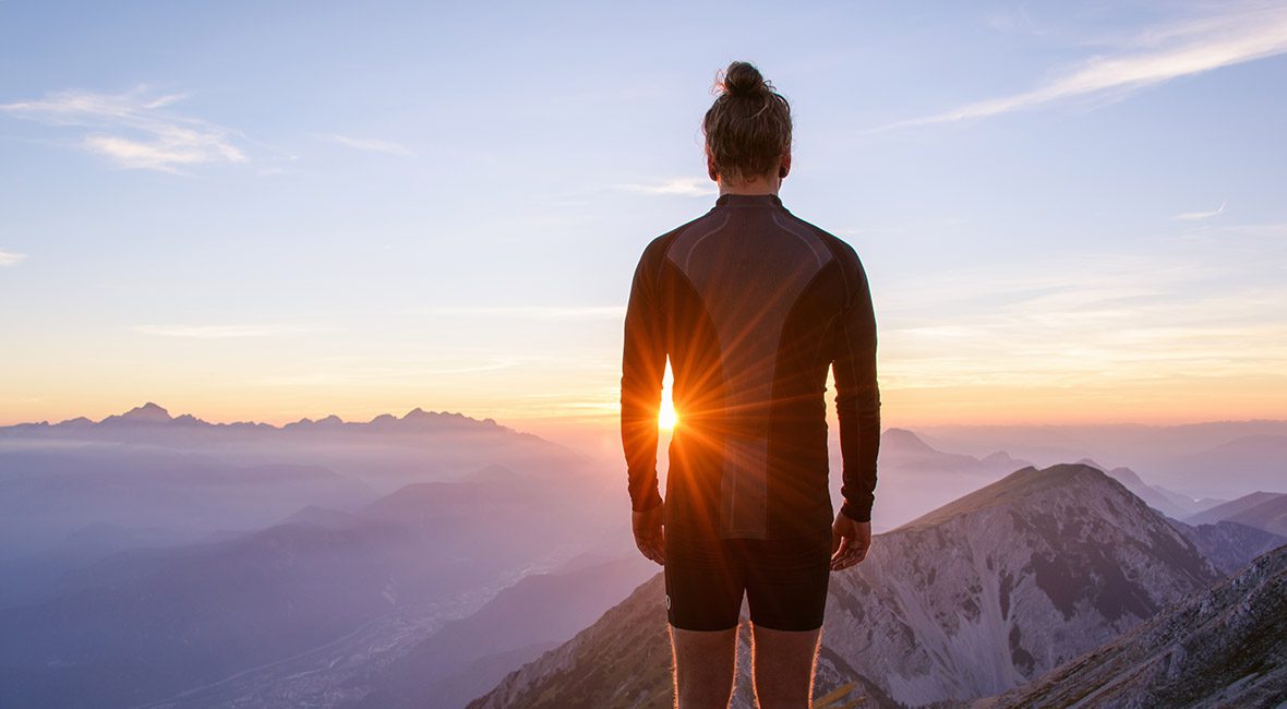 A person standing on top of a mountain at sunset.