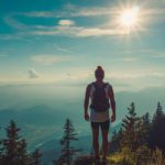 A person standing on top of a mountain with the sun shining.