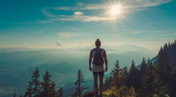 A person standing on top of a mountain with the sun shining.