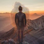 A person standing on top of a mountain at sunset.