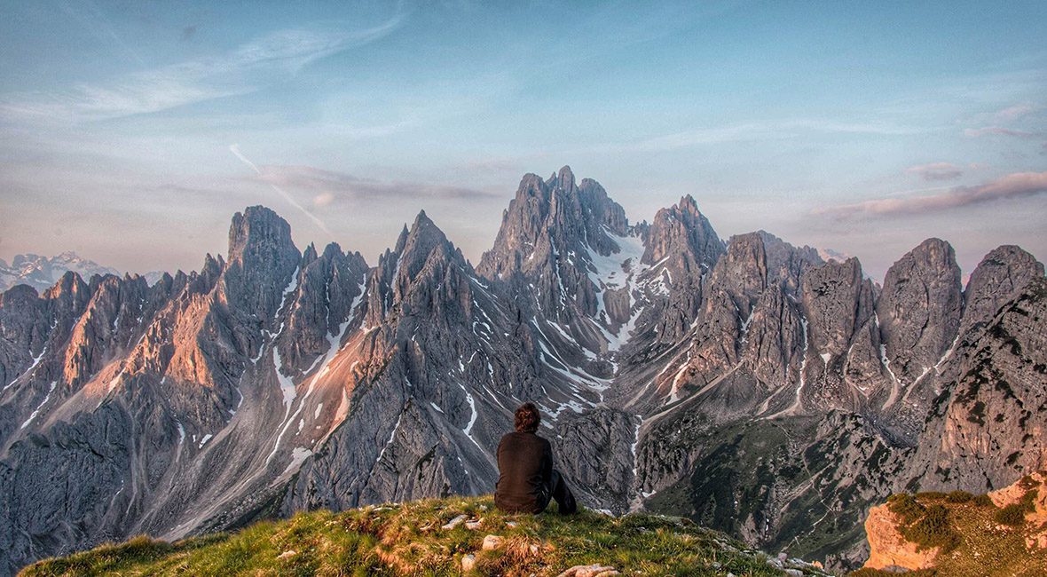 A person sitting on top of a hill looking at the mountains.