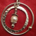 A silver circle with a pearl hanging from it.