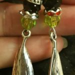 A hand holding two pairs of earrings with green and black beads.