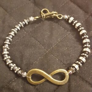 A gold infinity sign on a silver bead bracelet.