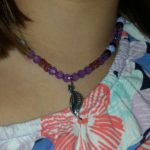 A woman wearing a necklace with purple beads and a leaf charm.