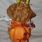 A pumpkin with leaves and a leaf sitting on top of it.