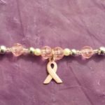 A pink ribbon charm is attached to the bottom of a beaded bracelet.