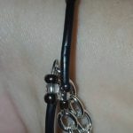 A close up of the wrist with a black leather bracelet and silver chain.