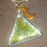 A green triangle shaped glass pendant with a gold moon charm.