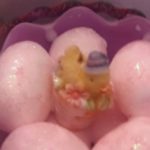 A close up of some pink eggs with a little chick on top