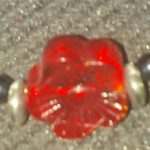 A red glass bead sitting on top of a gray carpet.