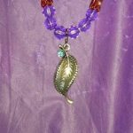 A purple necklace with a leaf pendant on it.