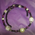 A purple and black necklace with pearls on it.