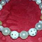 A white beaded bracelet with silver accents on a red cloth.